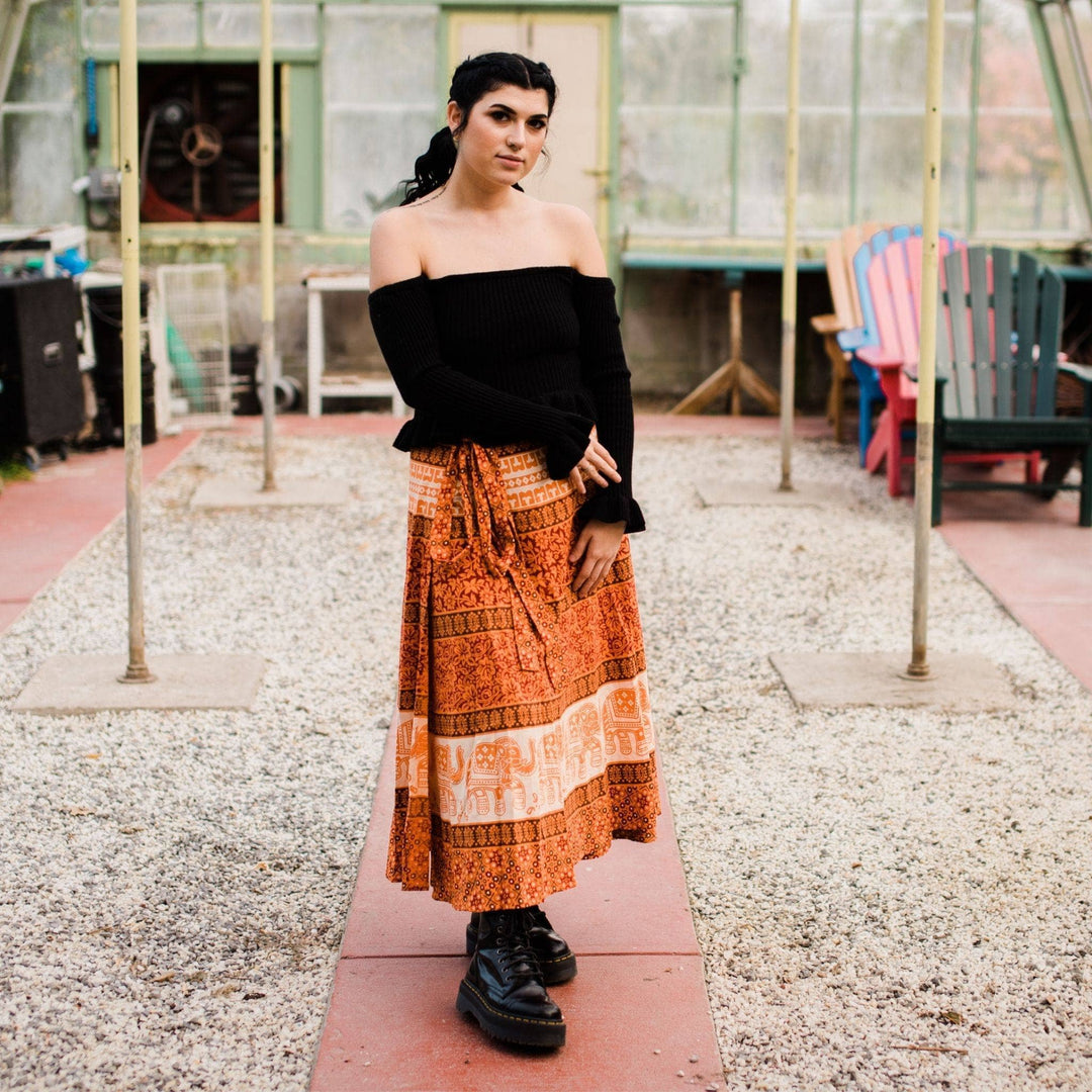 Model wearing orange cotton wrap skirt while standing in a greenhouse.