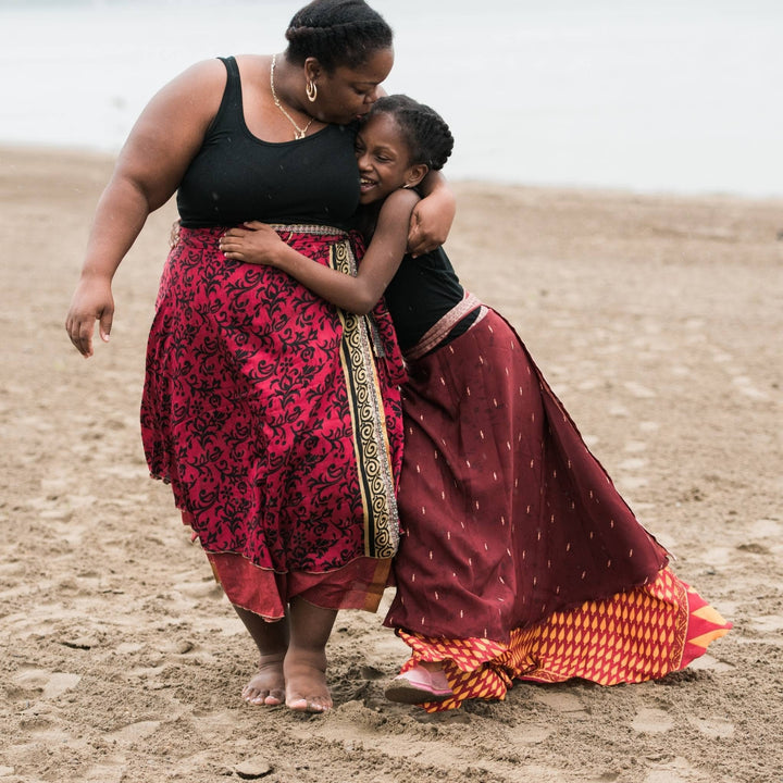 Two models walking on the beach. Adult model is wearing a red goddess maxi 100% sari silk skirt. 