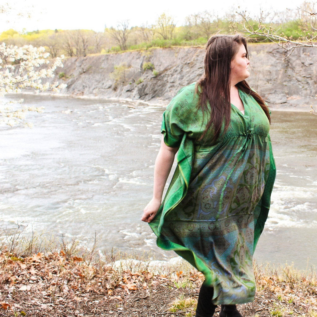 Model wearing sari silk maxi kaftan dress in green while standing outside with a river in the background.