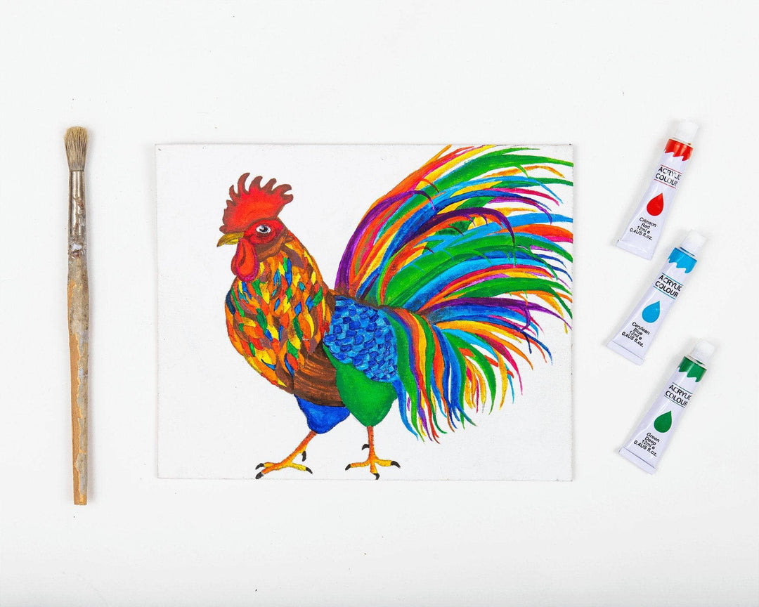 Paintbrush, complete painting of rooster, and 3 tubes of acrylic paint in front of a white background. Multicolor rooster painting was done by Jay B. Manager fo the DGY Warehouse.