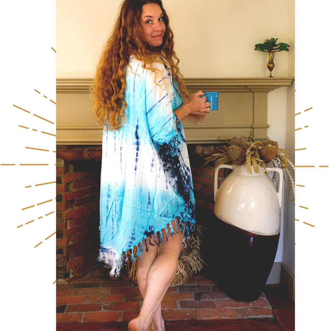 Nicole Snow wearing the tie dye sleep tunic in front of a fireplace, looking over her shoulder while holding a mug.