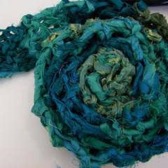 Sari Ribbon Scarf in teals rolled up on a white surface