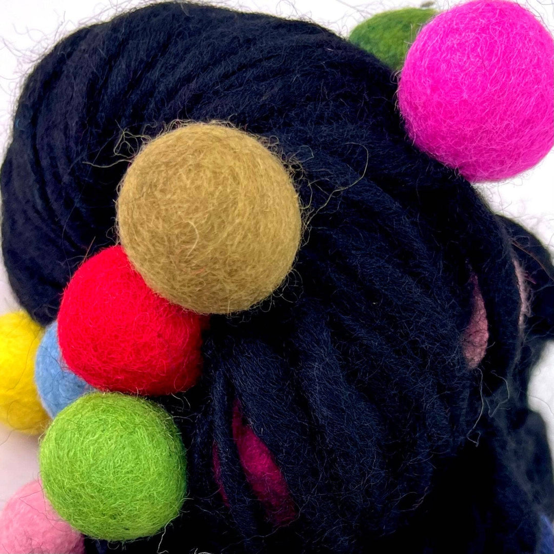 An up close view of the black felt ball wool yarn.  Showing the texture of the felt balls and the yarn. The felt balls are vibrant and rainbow in color.