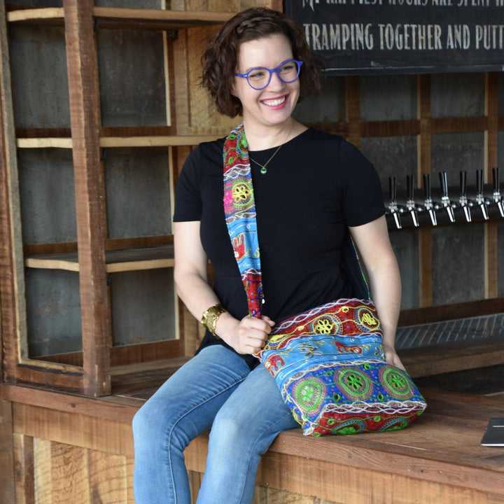Model sitting on a wooden bar wearing Journey through India Boho Sling Crossbody Bag. 