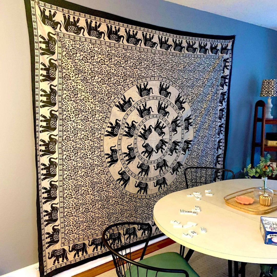 A Wandering Elephant Tapestry on a gray wall in a kitchen. There's a table with dominos on it in front of the wall hanging.
