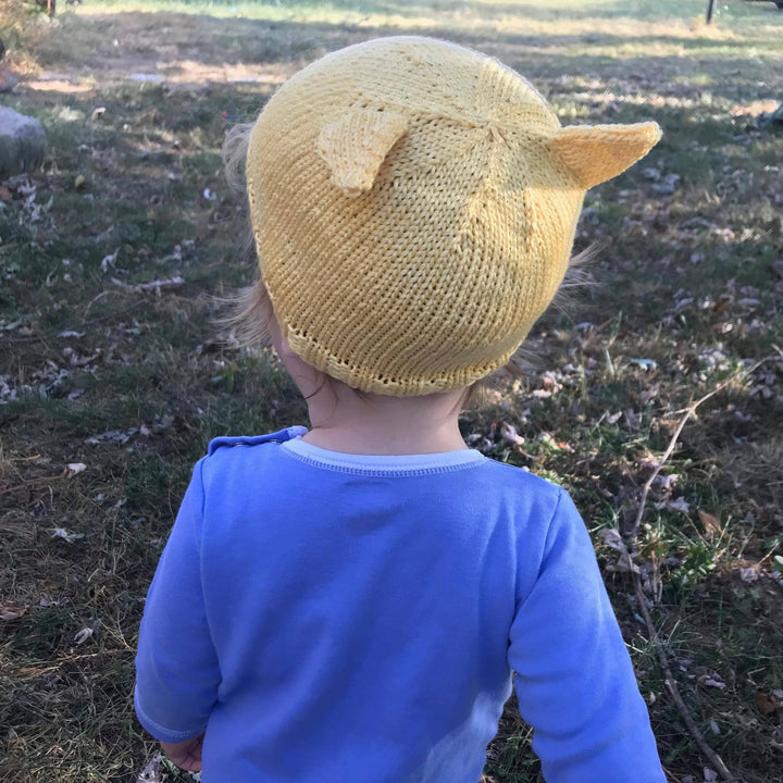 Child walking outside wearing a yellow cat ear beanie and wearing a purple shit