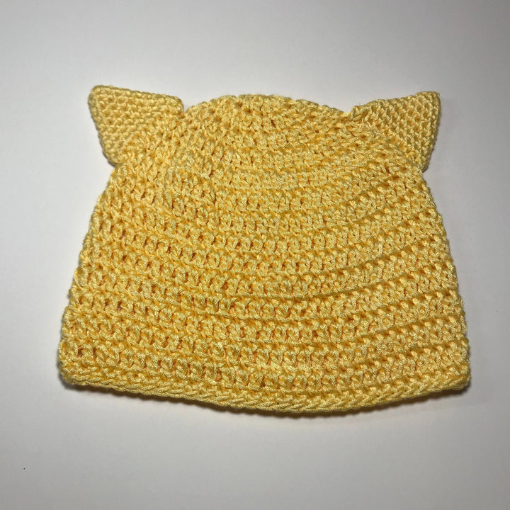 A yellow cat ear child beanie laying flat on a white background