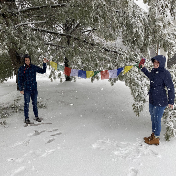 Multicolored Tibetan prayer flags outside on with a tree in the background with people holding the flags