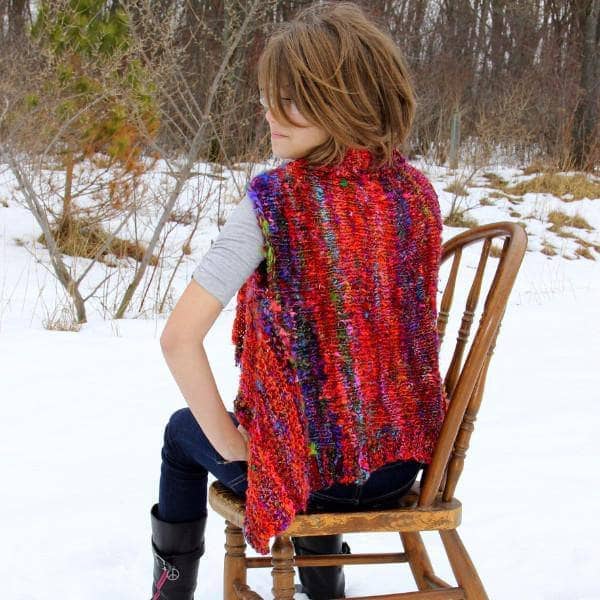 Woman wearing Adventure Cardi vest in multicolor sitting on a wooden chair in front of a snowy landscape