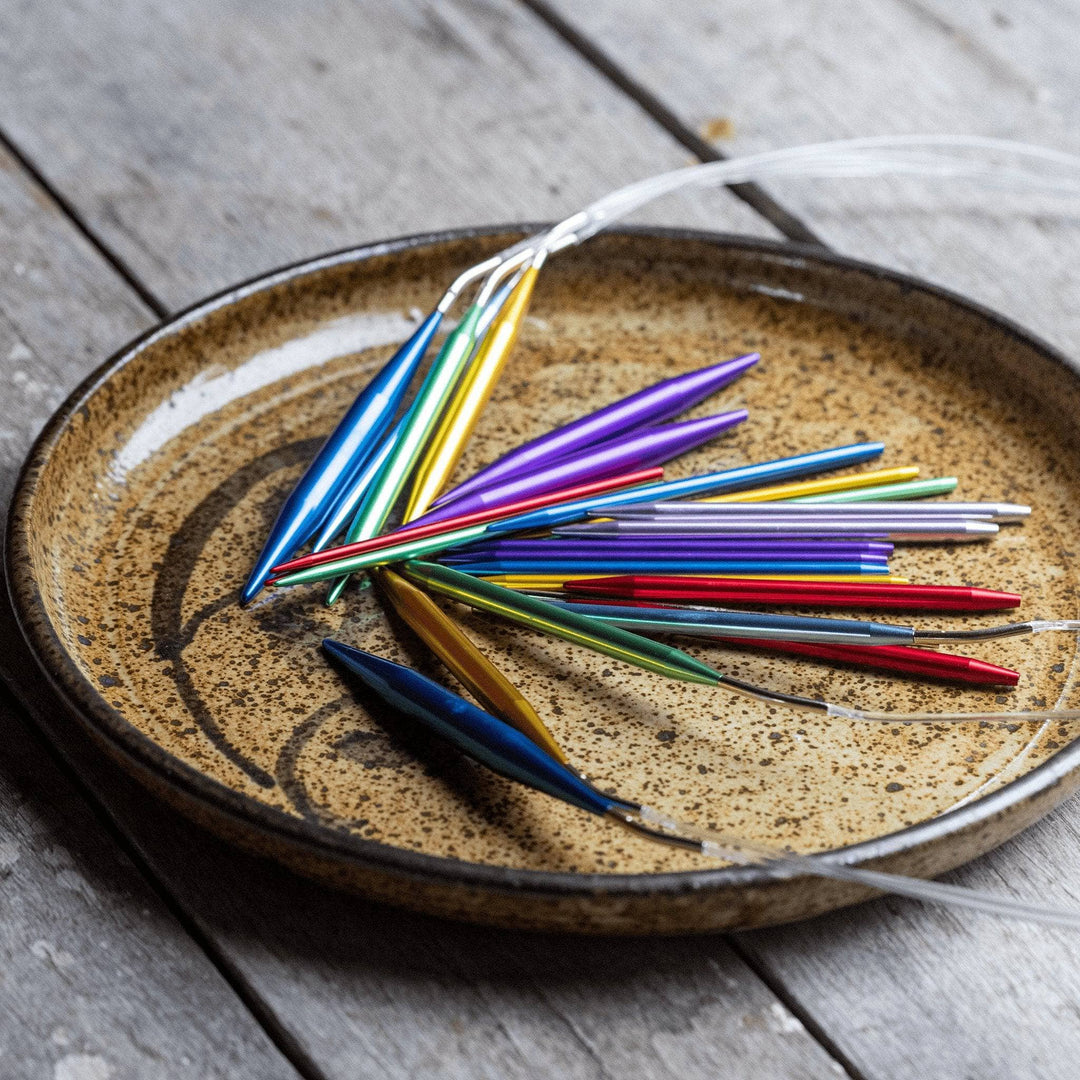 Aluminum interchangeable knitting needles on a stoneware plate in front of a distressed wood background.