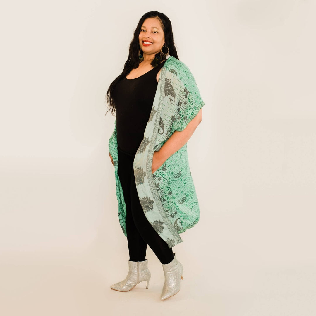 Plus size model has on a teal amara long duster while standing in front of a white backdrop. 