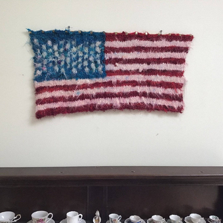 Knit American Flag hanging on a white wall above a brown china cupboard