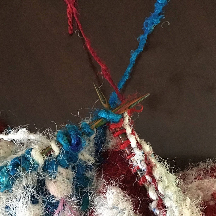 Red, white, and blue yarn on knitting needles over a brown background