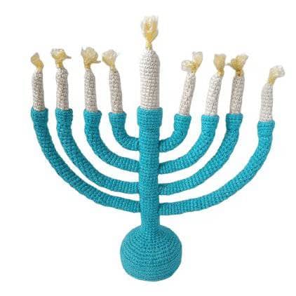 a plush blue menorah with white candles, and yellow flames made of yarn on a white background 