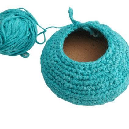A blue yarn menorah base with cardboard inside and a ball of blue yarn sitting on the left side, all on a white background