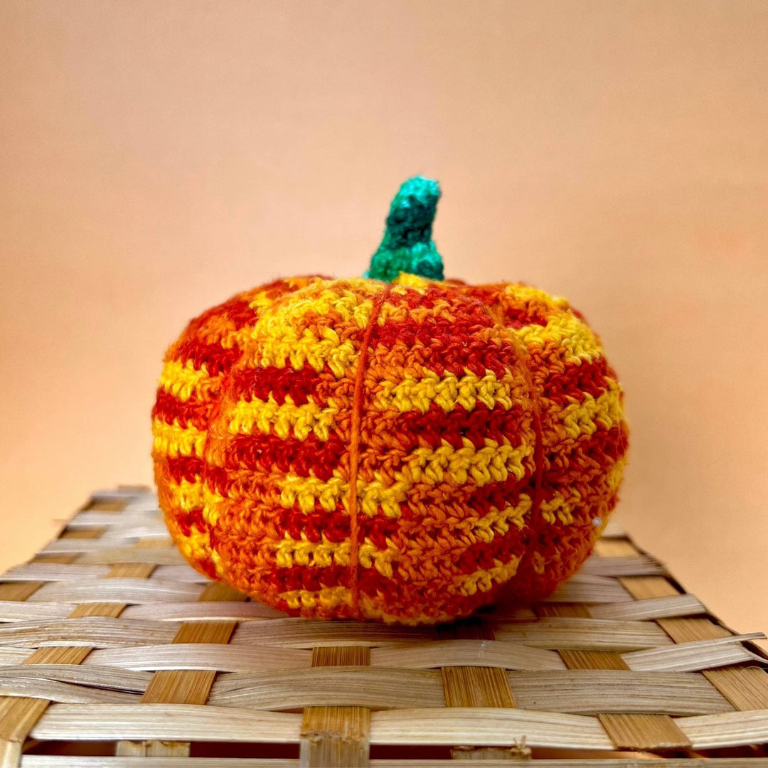 Closeup image of crochet amigurumi pumpkin sitting on basketweave in front of a peach background.