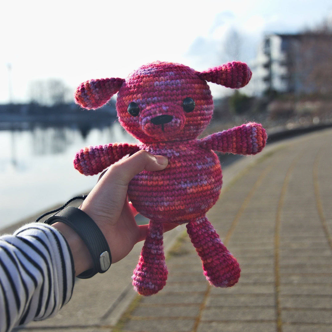Young girl's hand holding an Amigurumi Puppy crocheted in Raspberry (pinks)