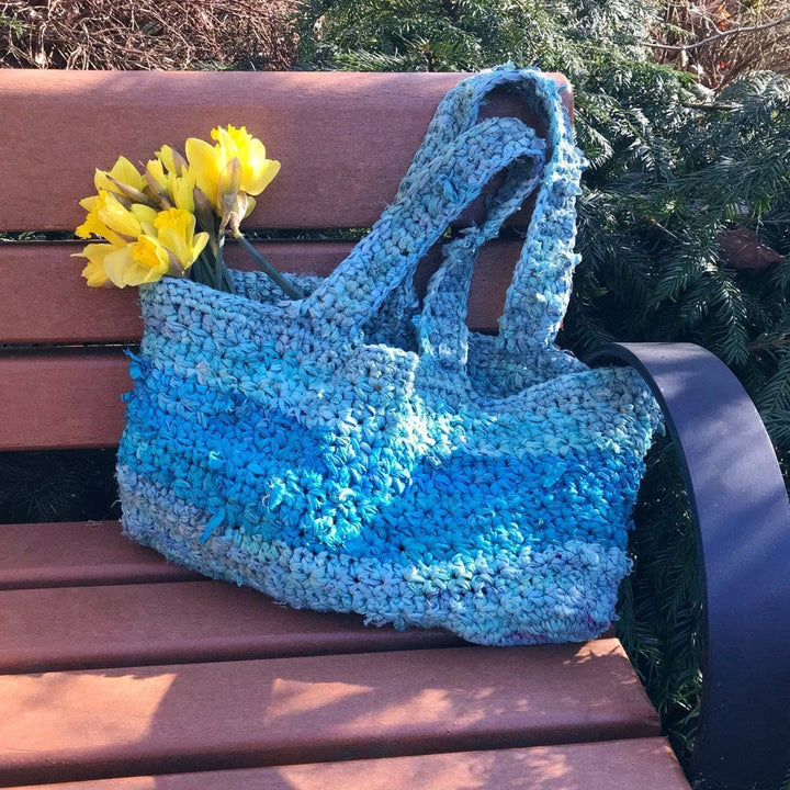 Anna Tote Bag crochet tote in blues sitting on a wooden bench