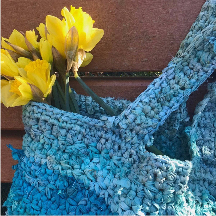 close up of Anna Tote Bag crochet tote in blues sitting on a wooden bench