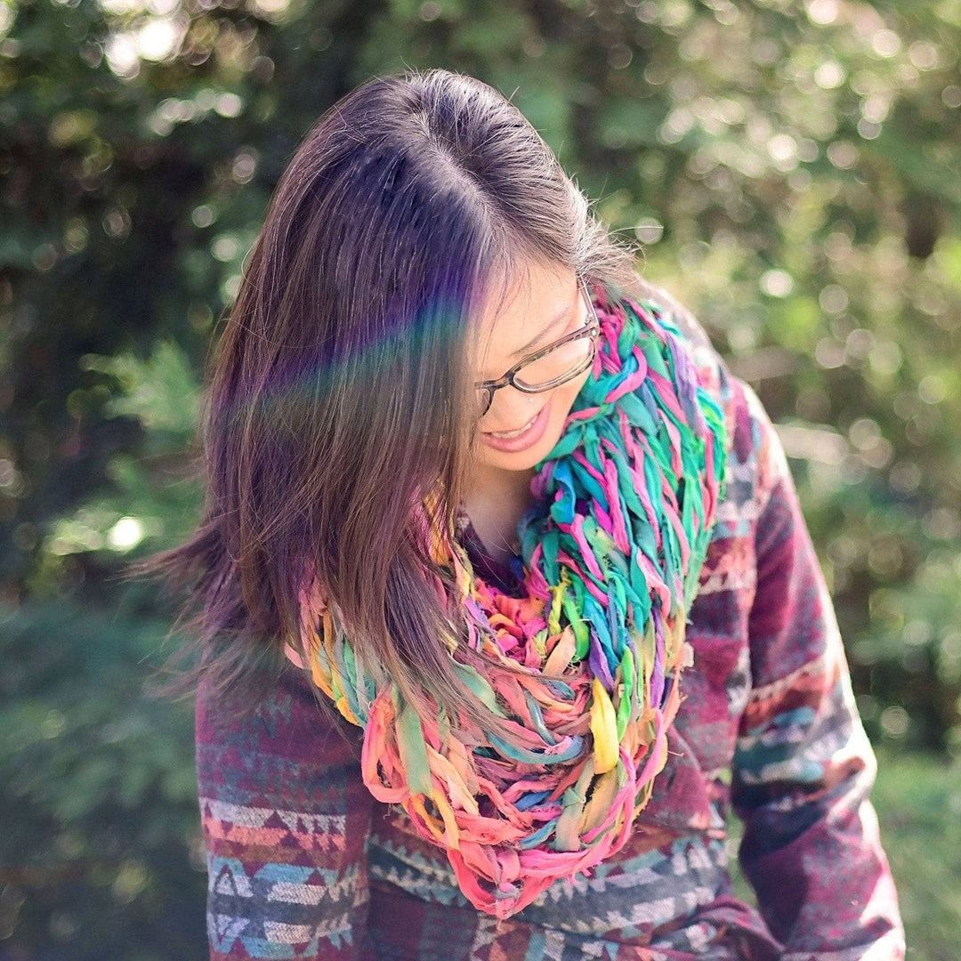 girl looking down wearing a multicolored scarf with trees in the background