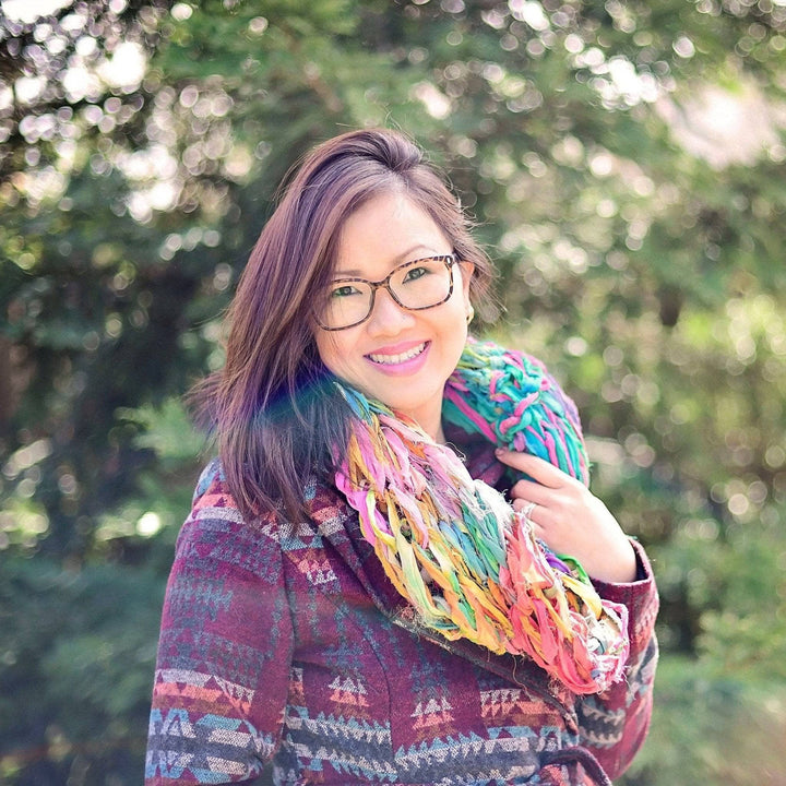 girl smiling wearing a multicolored scarf with trees in the background
