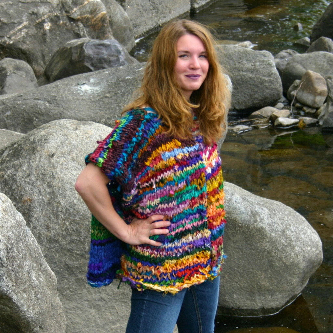 A woman standing on some rocks with her hands on her hips. She's wearing an Artfully Yours Poncho made from reclaimed sari silk ribbon