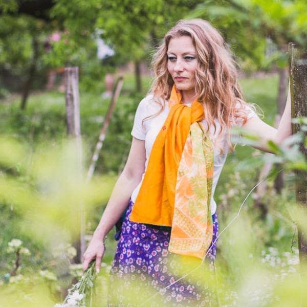 Woman wearing an Artisan Made Sari Silk & Cotton Scarf in yellow colors and standing in front of greenery