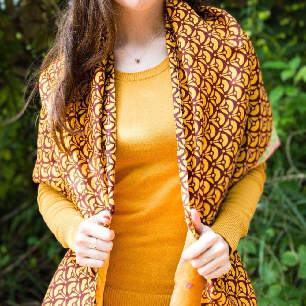 Woman wearing an Artisan Made Sari Silk & Cotton Scarf in yellow colors and standing in front of greenery