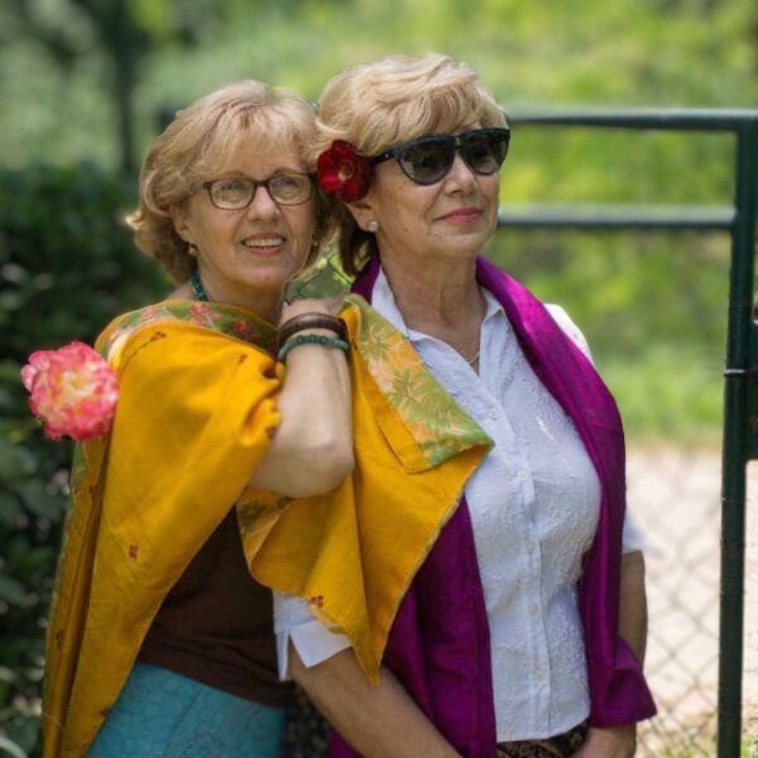 2 woman wearing Artisan Made Sari Silk & Cotton Scarves in pink and yellow colors and standing with each other in front of greenery