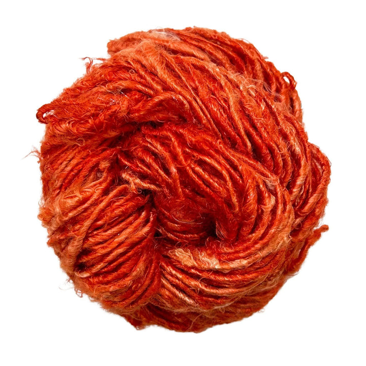 Top view of skein of Dusty Rose banana fiber yarn curled into a birds nest shape in front of a white background.
