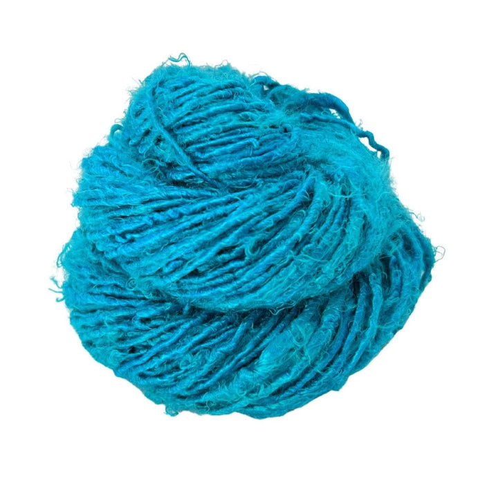 Side view of skein of electric blue banana fiber yarn curled into a birds nest shape in front of a white background.