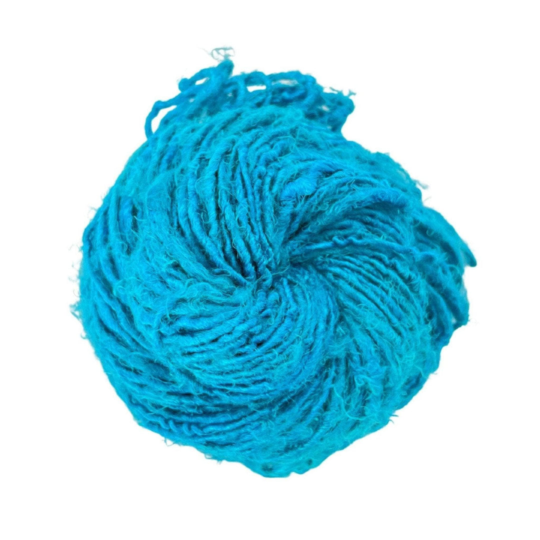 Top view of skein of electric blue banana fiber yarn curled into a birds nest shape in front of a white background.