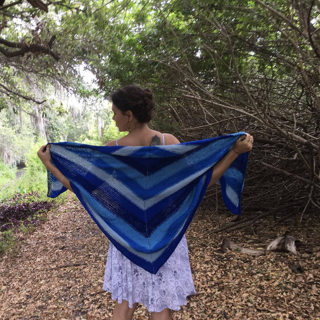 Designer standing in outside on a wooded path with multi hue blue shawl held out behind.