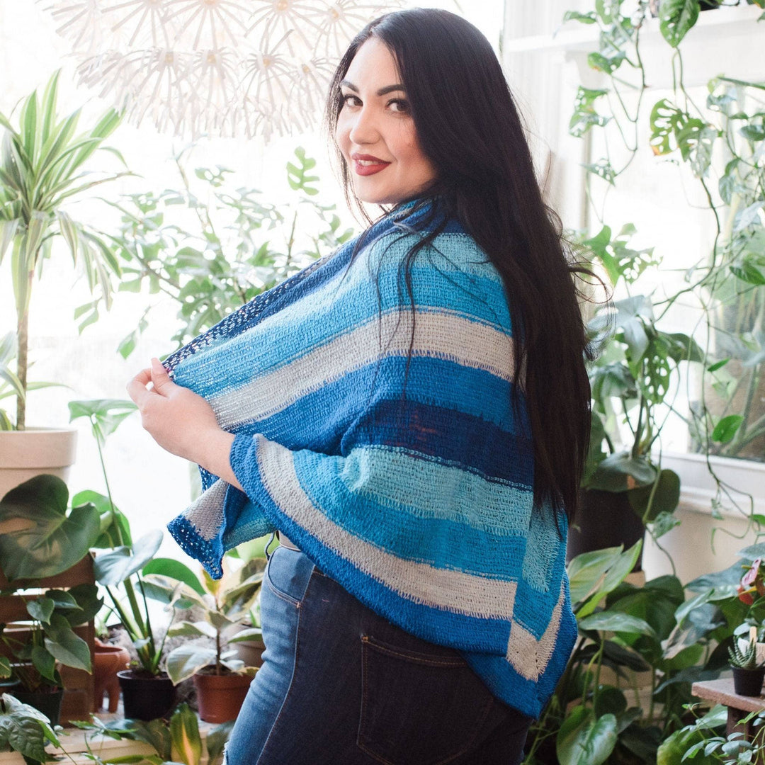 side view of model wearing I'm feeling plucky tunisian crochet shawl in blue with potted greenery in the background.