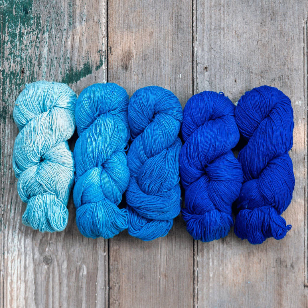 Ombre sport weight silk exploration pack in colorway blues (Left to right, light to dark) in front of a wooden background.