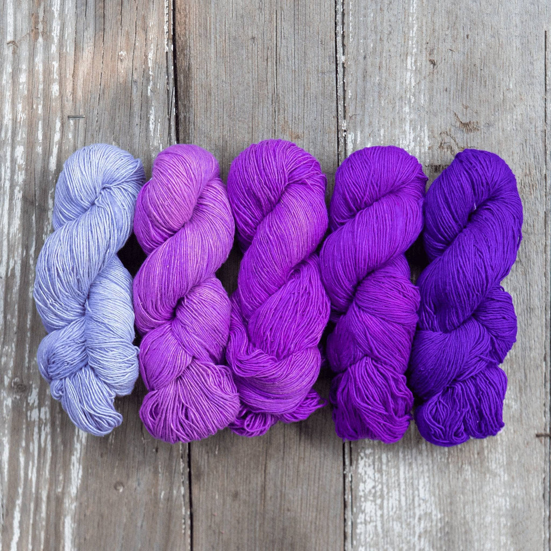 Ombre sport weight silk exploration pack in colorway purples (Left to right, light to dark) in front of a wooden background.