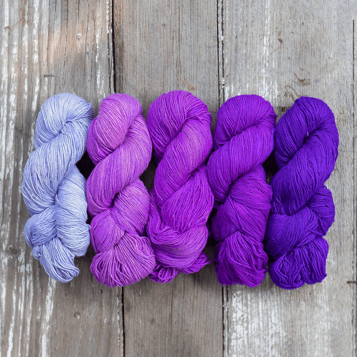 Ombre sport weight silk exploration pack in colorway purples (Left to right, light to dark) in front of a wooden background.