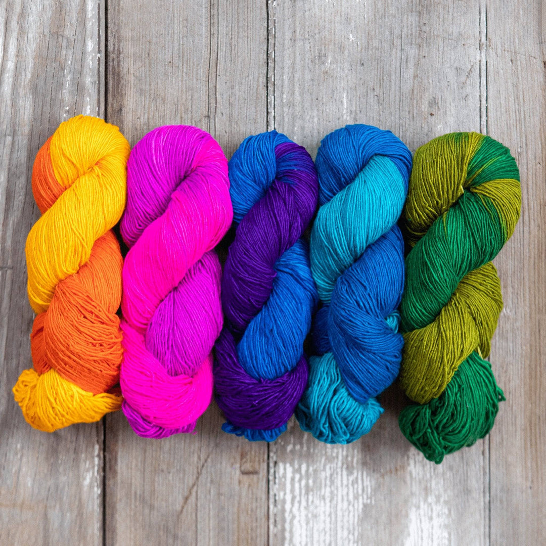 Ombre sport weight silk exploration pack in colorway rainbow (Left to right, yellow pink dark blue light blue green) in front of a wooden background.