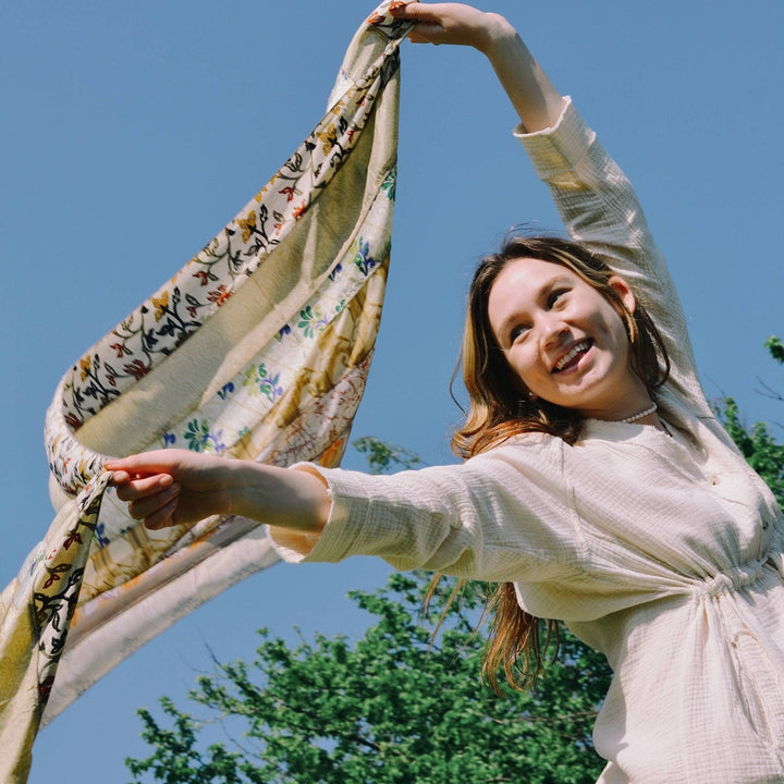Model is holding a white medley scarf in the air over their head. 
