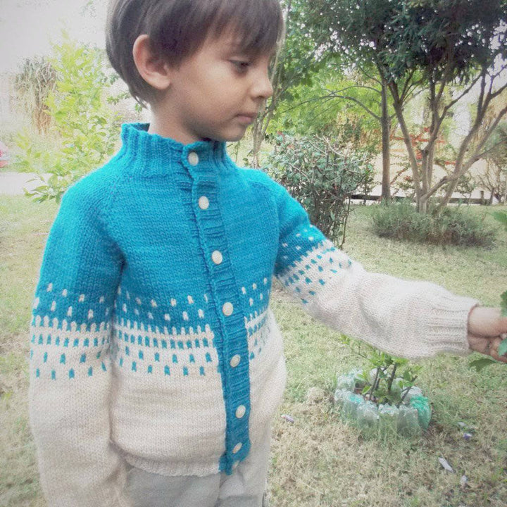 Child wearing Benja's Jacket knit sweater in blue and white and walking in a grassy area