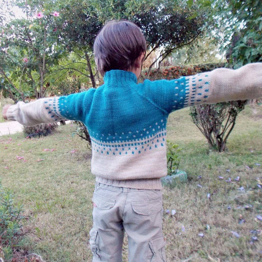 Child wearing Benja's Jacket knit sweater in blue and white and walking in a grassy area