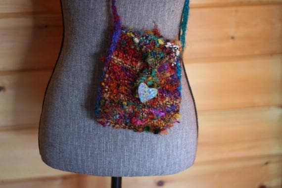 Gray mannequin wearing a multicolor mini knit purse standing in front of a wooden background