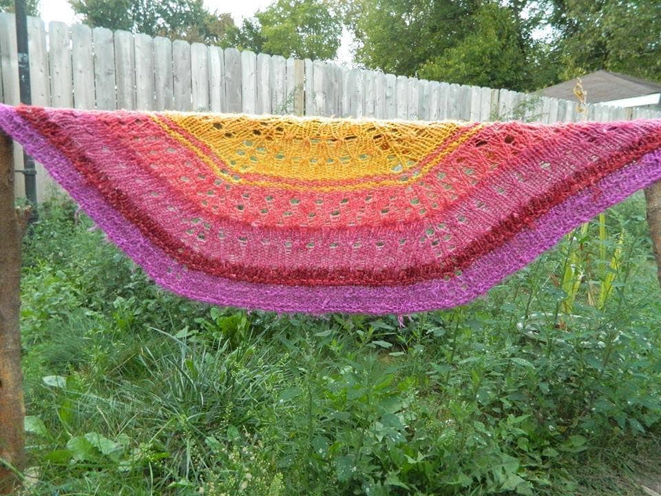 Pink and yellow semicircle shawl hung above a grass lawn 
