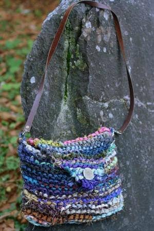 Small crochet crossbody clutch draped over a rock