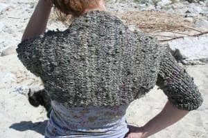 Back view of woman wearing a gray crochet bolero shawl sitting on a rock