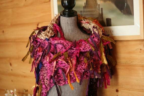 Mannequin wearing a hot pink fringe-y shawl against a wooden background