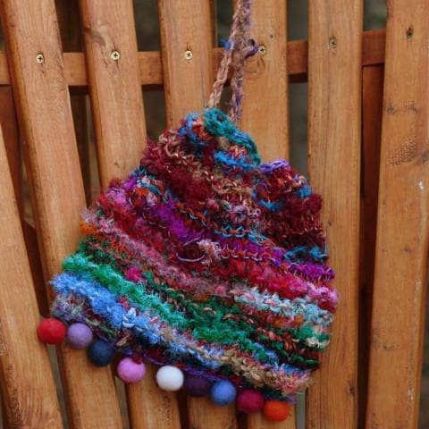 Blended Purse drawstring bag in multicolor hanging against a wooden wall