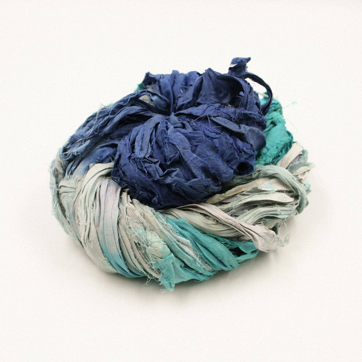a skein of blue, grey and light blue ribbon yarn on a white background