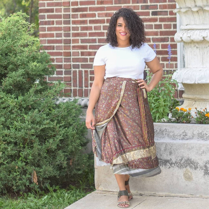 A woman wearing a patterned wrap skirt with a white shirt, standing near greenery.