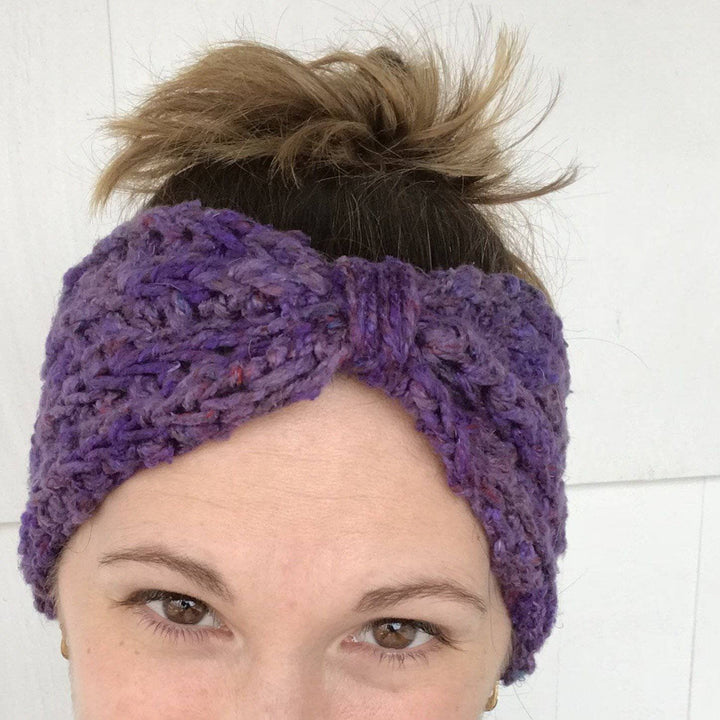 Woman's head wearing purple crocheted Bow Ear Warmer in front of a white background